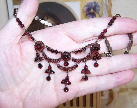 Dating to the late 1800s or so may I offer this breathtakingly beautiful Bohemian Garnet (points up) necklace from the Victorian era. With a wonderful festoon appearance, the metal of the necklace is thick with pale 9K rose gold (aka garnet gold - tested, not marked) - possibly over brass but I have the feeling the gold may be over silver. This is just a gut instinct which may or may not be right but I have not had a necklace like this with so much of a gold backing in a long, long time. Tongue-in clasp closure that works as it should. Neck length is 15-1/2"; center drop measures 1-1/2". Weight is 16.5 grams - quite a nice weight. Condition is excellent with no stones missing. I can spot perhaps (maybe) 2 replacements but again, I may be wrong on this. The back rose gold has mellowed quite Vintage Jewelry Necklaces, Whimsical Gothic, Gut Instinct, Festoon Necklace, Enchanted Wedding, Garnet And Gold, Vintage Jewelry Necklace, May I, Makeup Accessories