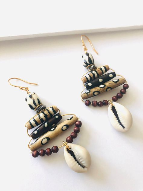 Standout from the crowd in these bold, unique statement earrings.  Materials: Wood, cowrie shell, bone Ear posts: Gold plated with clear ear backs (nickel free) Dimensions: Approximately 2.75" L x1.5"W Variation: All items are handcrafted, therefore size, shape, and color may vary slightly. Care: Take care when handling these pieces, they are built sturdily but still delicate and not unbreakable. The colors displayed may be slightly different due to your monitor's color calibration and resolution settings. Every attempt has been made to represent the product and features as accurately as possible. Thank you for shopping Soul Series Jewelry and supporting small business. Ready to ship. African Bead Jewelry, African Earrings Ethnic Jewelry, Earrings With Shells, Cowrie Shell Jewelry Necklaces, Diy Statement Earrings, African Style Earrings, Simple Beaded Earrings, African Jewelry Earrings, Afro Jewelry