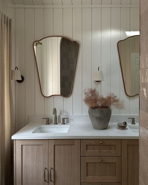 Cottage Living in the City | The existing bathroom had tall ceilings and a beautiful skylight but lacked storage and functionality. For the design, we decided to clad all the walls and ceiling in shiplap, adding to the height and volume of the bathroom! Due to the tight project timeline, we sourced a premade vanity but upgraded it with beautiful antique brass hardware and fixtures. We added intricate and dreamy details like curved mirrors, vintage sconces with fabric shades, and full-length... Slanted Ceiling Bathroom Vanity, Tall Bathroom Ceiling, Paneled Bathroom Walls, Horizontal Shiplap Bathroom, Shiplap Ceiling Bathroom, Full Length Bathroom Mirror, Wall Paneling Bathroom, Shiplap In Bathroom, Cottage Bathroom Vanity