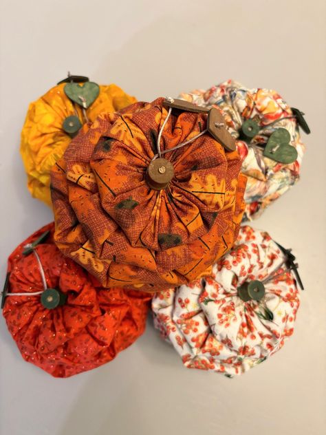 This is a small fabric pumpkin that would be perfect sitting on a shelf as part of your fall decor. Purchase a bowlful to make a beautiful fall centerpiece.  It is slightly larger than an average apple, and it can be purchased in five different fall prints.  It is made by placing increasing and decreasing sized yo-yo's that are stuffed with polyester fiberfill. The yo-yo's are placed on a 1/8 inch dowel that has a small wooden wheel on the bottom.  It is finished with a wooden spool and two pain Yo Yo Pumpkins, Yoyo Pumpkins, Quilted Pumpkins, Yo Yo Crafts, Fall Rec, Fabric Yoyos, Fall Creations, Primitive Scarecrows, Americana Crafts