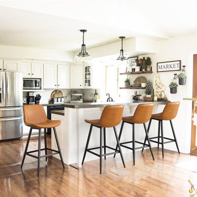 These counter stools bring a modern industrial vibe to your kitchen island or bar area. They arrive in a set of four, and they're crafted with an iron frame and splayed legs in your choice of neutral finish. The bucket-style seat with low backrests are wrapped in foam-filled faux leather upholstery for lots of cushioned support while you enjoy meals and conversation with friends and family. We also love how the wraparound footrests keep your feet cozy, too. Plus, the plastic glides on the legs h Modern Bar Stools Kitchen, Counter Stools With Backs, Brown Bar Stools, Island Stools, Bar Stools Kitchen Island, Leather Kitchen, Stools For Kitchen Island, Leather Counter Stools, Counter Bar