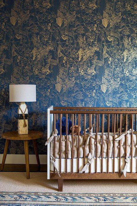 Eclectic boy's nursery features a wall clad in blue and gold print wallpaper lined with a mid century modern crib next to a tripod accent table topped with a painted driftwood and rope lamp alongside a blue kilim rug layered atop a cream wool rug. Moody Nursery, Eclectic Nursery, Kindergarten Wallpaper, Modern Crib, Baby Wallpaper, Beautiful Nursery, Nursery Wallpaper, Nursery Inspiration