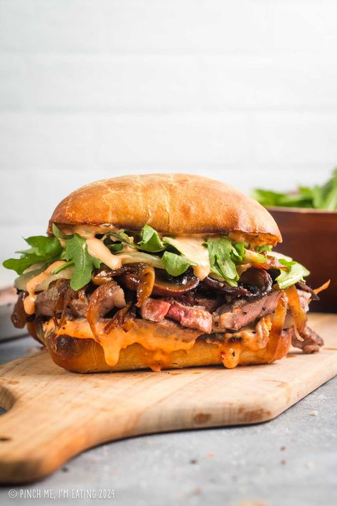 This grilled ribeye steak sandwich is loaded with roasted red pepper garlic aioli, arugula, provolone, caramelized onions, and mushrooms, all on a toasty ciabatta roll. You can even use thinly sliced leftover steak in this recipe! This sandwich is a great main course dish, and the sauce is out of this world! Sandwich Recipes With Arugula, Bistro Recipes Dinners, Hot Dinner Sandwiches, Steak And Pepper Sandwiches, Vegitaren Recipes Sandwiches, Best Steak Sandwich Recipe, Steak Ciabatta Sandwich, Fall Steak Recipes, Summer Meat Recipes