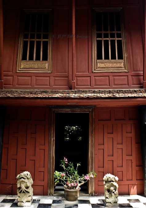 One doorway to the Jim Thompson house in Bangkok.  Potted plant centered in the doorway (visitors are not supposed to use it) flanked by two ancient dragon sculptures.  The house walls are red-toned wooden panels in traditional Thai style. Bangkok Tourist, Jim Thompson House, Tropical Colonial, Bangkok Shopping, Colonial Interior, Thai House, Jim Thompson, Ancient Dragon, Bangkok Hotel