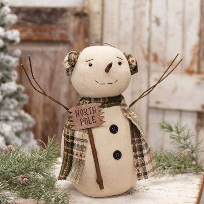 North Pole Snowman Doll is a decorative stuffed fabric sitter made with primitive seasonal style. The doll wears a green plaid scarf with matching earmuffs and holds a rustic wooden sign that reads, "North pole." The snowman features flexible wire arms and two button accents. A weighted bottom allows for freestanding display on a flat surface. Measures 11.5" high by 10" wide by 5.5" deep with outstretched arms. The Holiday Aisle® | The Holiday Aisle® North Pole Snowman Doll 11.5 H x 5.5 W x 5.5 Crafty Christmas Gifts, Fabric Snowman, Green Plaid Scarf, Snowman Doll, Crafty Christmas, Rustic Wooden Sign, Snowman Crafts, Fabric Christmas Ornaments, The Snowman