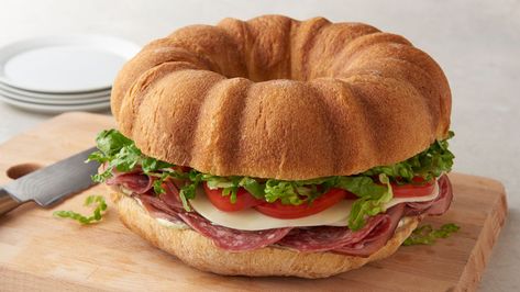 Forget about spending cash on subs in bulk from the sandwich shop. This crazy-good recipe makes feeding a crowd totally easy, but will also get you some serious oohs and aahs. We call it: the "Bundtwich." All of your favorite Italian sub ingredients (like smoked ham, salami, provolone and pesto mayo) get sandwiched between two French loaves baked in a bundt cake pan for a giant sandwich that’s ready to party! Sandwich Rings French Bread, Bundt Sandwich Ring, French Bread Bundt Pan Sandwich, Bundt Pan Sandwich Ring, Pillsbury French Bread Recipes, Giant Sandwich, Pesto Mayo, Bundt Pan Recipes, French Loaf