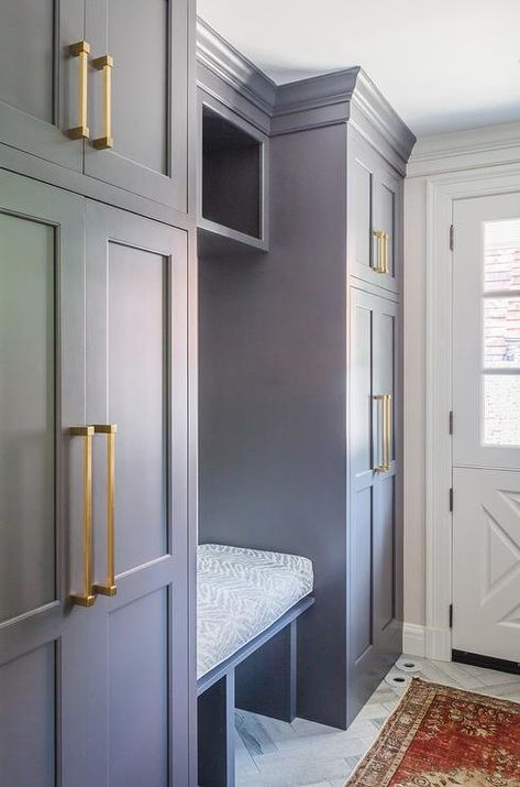 Floor to ceiling gray cabinets accented with brass pulls are fixed on either side of a gray shelf located over a gray built in bench finished with a white and gray cushion. Dark Gray Mudroom, Gray Mudroom Cabinets, Gray Mudroom, Grey Cupboards, Mudroom Cabinets, Mudroom Flooring, Grey Shelves, Mudroom Lockers, Grey Kitchen Designs