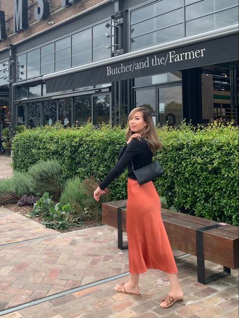 Woman in front of shops with hedge, dressed in autumn style clothing - long orange skirt midi length with black long sleeve half turtle neck top holding a 90’s style handbag and brown slides or sandles, posing looking back Orange Midi Skirt Outfits, Midi Skirt Outfits, Long Skirt Outfit, Orange Midi Skirt, Style Midi Skirt, Midi Skirt Outfit, Long Skirt Outfits, Modest Fits, Orange Top