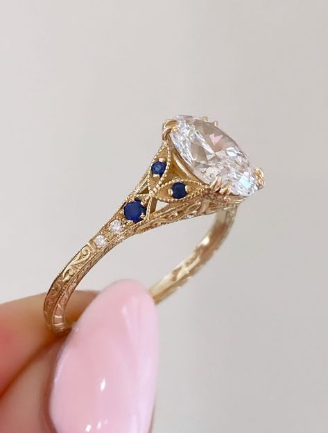 Skyla - Sapphire is a timeless masterpiece that captures the essence of romance and elegance. Its enchanting silhouette features delicate curves and ornate embellishments with three vibrant blue sapphires are set on either side of her oval heart for a regal pop of color. Islet's curved band holds a marquise diamond as the center piece accompanied by two baguette cuts on either side with round cut sparklers finishing off the piece. Natali - Curved completes the stack with a gentle hug of diamonds Luxury Vintage Sapphire Engagement Ring, Three Wedding Bands, Diamond Ring With Colored Side Stones, Cool Rings Women, Vintage Wedding Rings Sapphire, Wedding Rings Engagement Oval Gold, Dual Engagement Rings, His And Hers Wedding Rings Sets, Secret Garden Ring