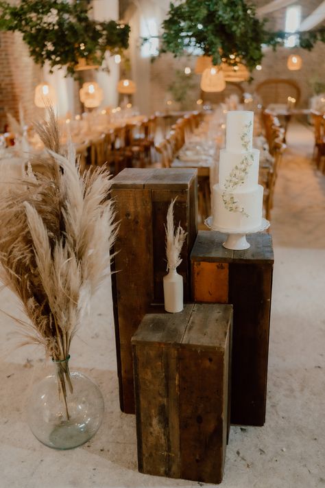 This shows a rustic cake display. Featuring our wooden plinths in three different heights, on the middle plinth is a white three tiered wedding cake on a white cake stand. Alongside the plinth is a large vase of dried pampas. In the background is a rustic dining set up. Wedding Plinths Ceremony, Cake Station, Rustic Ceremony, Wooden Plinth, Barn Photography, Floor Boards, Antique Flooring, Event Display, Ceremony Design