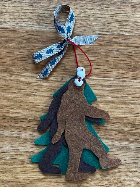 "Stand quietly under the magical Sasquatch mistletoe, close your eyes, and wait... you're sure to get a smooch. Hand-made felt Bigfoot and tree shapes in brown and green. Tied together with white wooden \"berries,\" a red thread hanger, and a festive seasonal bow. This awesome artwork is 3 great things in one: doorway hanger, Christmas tree ornament, and gift tag! Get a bunch to share with friends." Scout Christmas Ornaments, Funny Felt Ornaments, Scout Christmas Crafts, Felt Bigfoot, Sasquatch Ornament, Diy Mistletoe, Mistletoe Diy, Bigfoot Ornament, Hanger Christmas Tree