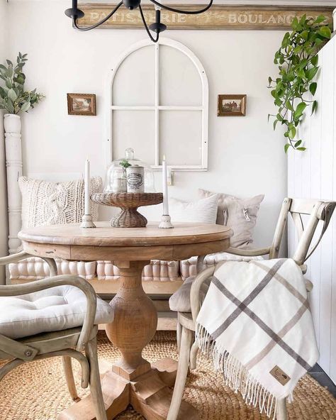 Get cozy in this small breakfast nook featuring a round light wood farmhouse dining table. The table stands on a round jute rug in front of a light wood bench with beige tufted seat cushions. Pair the bench with wooden dining chairs for a cozy place to enjoy your morning coffee. Round Wood Farmhouse Table, Cottage Dining Room Round Table, Round Table Breakfast Area, Round Table Dining Nook, Light Wood Round Dining Table, Round Breakfast Table Ideas, Farmhouse Eat In Kitchen, Dining Chairs Round Table, Light Wood Farmhouse