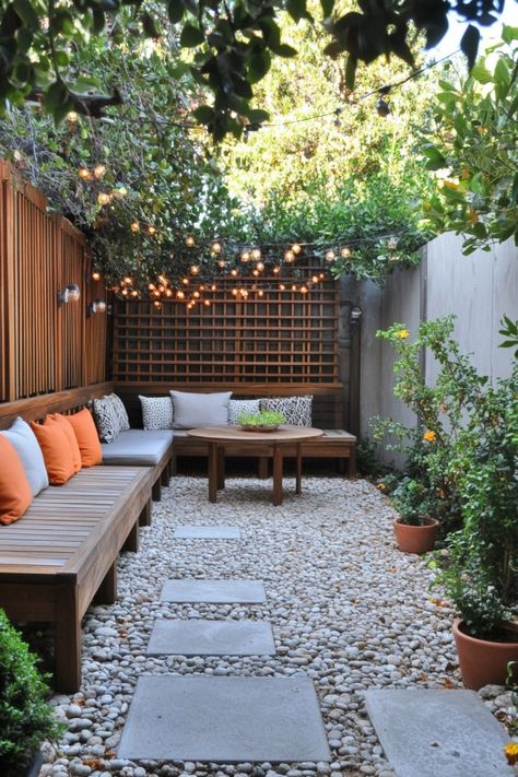 Cozy outdoor patio with string lights, wooden seating, orange and gray cushions, potted plants, and a stone pathway. Small Round Patio Ideas, Small Patio Pavers Design, Patio On Side Of House, Painted Patio Ideas, Small Deck Inspiration, Small Patio Oasis Ideas, Cement Slab Patio Ideas, Small Patio Design On A Budget, Covered Patio Design On A Budget