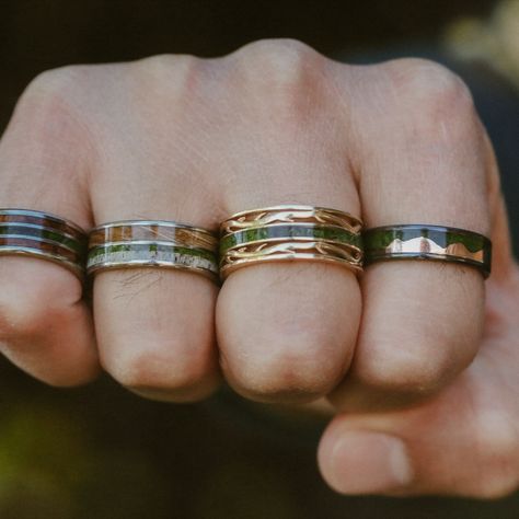 Eight different moss wedding bands from Staghead Designs are shown on a man's left and right hands. These designs include "Vega" flat top band in white gold with moss & ironwood, "Ezra" with moss mountains & whiskey barrel oak, "Rio" with moss, camo, & elk antler, "Remmy" with redwood & moss, "Rio" with moss & redwood, "Dyad" with whiskey barrel, moss, & antler, "Artemis" antler-style band with moss, & "Helios" with moss & rose gold mountains. Moss Agate Mens Wedding Band, Moss Agate Mens Ring, Unique Male Wedding Bands, Moss Agate Wedding Rings, Earthy Wedding Rings, Moss Agate Engagement Rings, Agate Engagement Rings, Earthy Rings, Boho Wedding Bands