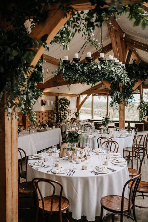 How stunning is this rustic barn wedding set-up for Zoe and Joe's real wedding in the Cotswolds! We love this hanging foliage from the candelabras and beams, plus the wildflower displays on the tables. This is the perfect example of rustic wedding decor. Country Wedding Set Up, Rustic Wedding Set Up, Beam Wedding Decorations, Wedding Beam Decoration, Wedding Reception Ceiling Decorations Rustic, Flowers On Beams Wedding, Wedding Venue Flowers Hanging, Barn Wedding Hanging Flowers, Long Rustic Barn Wedding Tables