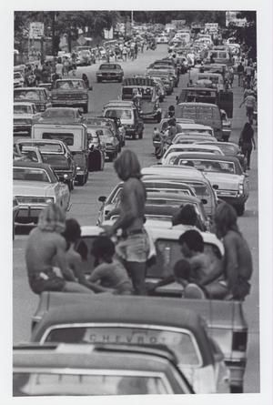 Photograph of a line of cars and people waiting for entry to an unidentified music festival. Bumper-to-bumper traffic sits long enough for people to sit on and hang out of vehicles. Many individuals choose to enter the festival on foot and are visible in lines on either side of the road. Austin Neighborhoods, Zilker Park, Railroad Companies, Texas Photo, Retro Film, Downtown Austin, School Building, The Festival, The 1970s