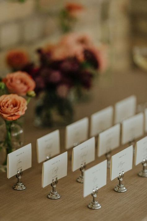 Minimal escort card display with silver harp stand and floral bud vases behind. Wedding Place Card Table Display, Placecards Wedding Table Display, Bookmark Table Cards, Elegant Seating Chart Wedding, Table Placecards Wedding Card Displays, Postcard Wedding Table Numbers, Floral Bud Vases, Hermitage Hotel, Winnipeg Wedding