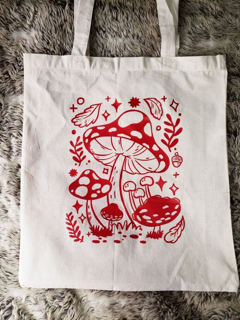 This Mushroom tote bag is perfect for carrying around those little extra bits whilst out and about.  The design is printed with htv vinyl, onto a cotton canvas tote bag. The bag is roughly 40cmx35cm big. (Washing instructions are provided with the bag). All bags are printed and pressed by hand, so may vary slightly. Please feel free to message me if you have any questions at all Canvas Bag Design Diy, Tote Bag Print Design, Cute Tote Bag Design, Tote Bag Design Ideas, Mushroom Canvas, Bag Design Ideas, Decorated Tote Bags, Mushroom Tote Bag, Painted Canvas Bags