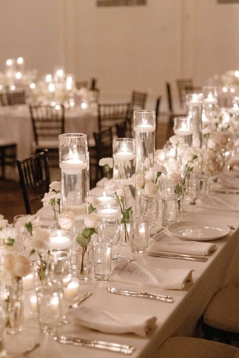 A stunning reception setup featuring delicate white florals and glowing candlelight, creating an atmosphere of romance and sophistication. Perfect for a timeless wedding celebration. #CandlelitWedding #ElegantReception #WhiteFlorals #RomanticAmbiance #WeddingInspiration White Candle Lit Wedding, White And Candle Wedding, Wedding Round Table Candles, Small Indoor Reception, Candle Decor For Weddings, Reception Set Up, Reception Table Decorations Simple, Classy Indoor Wedding, Wedding Table With Candles