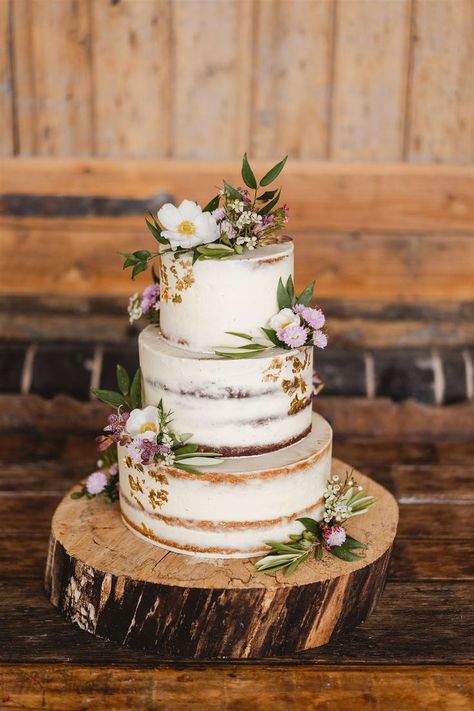 Rustic semi naked wedding cake with flowers and buttercream on a log slice cake stand www.samandlouise.co.uk Rustic Cake Flowers, Rustic Tiered Cake, Rustic Flower Wedding Cake, Rustic Carrot Cake Wedding, Distressed Wedding Cake, Wedding Cake On Log Slice, Wedding Cake At Home, Log Cake Stand Wedding, Boho Simple Wedding Cake