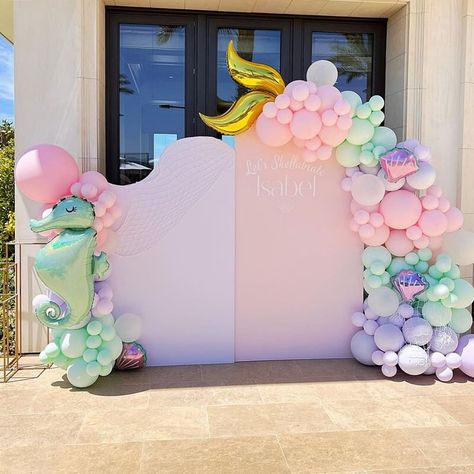 Create a sweet and adorable under the sea themed party backdrop and make an impressive impression on your guests. Set white and pink backdrop stands and beautifully decorate them with pastel pink, lavender, mint balloon garland and add sea shell & sea horse shaped balloons to make your backdrop more adorable. Spread decorative fish net on the balloons and backdrop stand and place gold column stands in various heights to enhance the elegance of your under the sea party backdrop. Under The Sea Balloon Backdrop, White And Pink Backdrop, Mint Balloon Garland, Under The Sea Balloon Arch, Under The Sea Backdrop, Under The Sea Themed Party, Event Decor Ideas, Party Decorations Table, Backdrop Stands