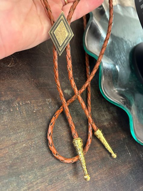 This awesome bolo tie has a metal diamond design. The cord is genuine brown leather. Our bolos pair nicely with many of our belt buckles! They make wonderful gifts.    The western bolo tie rope length is 39'' ; charm pendant size is 1 1/4'' tall Men’s Bolo Tie Wedding, Gold Bolo Tie, Bolo Ties For Men, Cowboy Necktie, Bolo Tie Men, Casual Groom Attire, Necklace Leather Cord, Casual Grooms, Western Bolo Tie