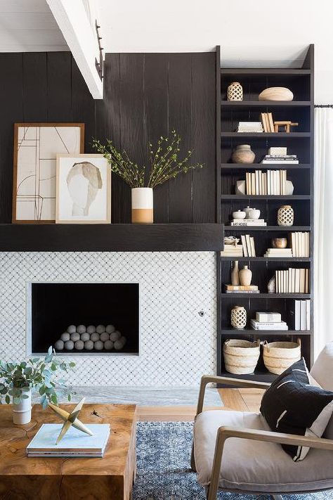 A styled ebony-stained bookcase is built-in beside a fireplace boasting white quatrefoil surround tiles and an ebony-stained mantel topped with layered art placed against an ebony-stained wood plank fireplace wall. Furnitur Ruang Keluarga, Tile Fireplace, Shiplap Fireplace, Bookshelves In Living Room, Wood Beam Ceiling, Design Salon, Neutral Living Room, Brown Living Room, Wood Coffee Table