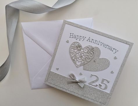 Handmade silver wedding/anniversary card.  Two intertwined hearts, one silver glitter and one die cut, surrounded by tiny silver hearts, a silver satin bow and a silver glitter background.  Wording is 'happy anniversary' printed in silver.  Card insert reads 'congratulations' in silver.  #greetingcards #silverwedding #creative #anniversary #cards #gifts #handmade #hearts #glitter card stock #silver #celebration#25years Creative Anniversary Cards, Silver Glitter Background, Silver Wedding Cards, Engagement Anniversary Card, Silver Card, Intertwined Hearts, Anniversary Cards Handmade, Wedding Anniversary Card, Silver Wedding Anniversary