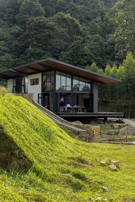 The one-and-a-half storey, 1600-sq-ft abode adopts the stance of a hillside cabin albeit without the steep inclines and overt vernacular overtones. Its modernist rectilinear form is stilted like a traditional Malay kampung house, and immense two-tier platform thrusts over lawned terraces in frozen inertia. A corresponding pitched roof, with its 3.5-metre cantilever, enhances that captured movement to create the cabin’s dynamic silhouette. House Design Steep Slope, Flat And Slope Mixed Roof Design, Steep Hillside House, Buildings On Slopes Architecture, House On Slope Architecture, Houses On Steep Slopes Architecture, House On The Hill Architecture, Kampung House, Hillside Cabin