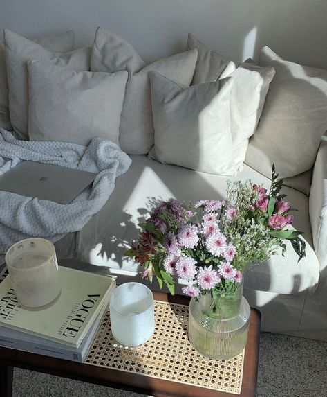 A white couch coating in sunlight. There’s a coffee table with hooks, candles, and a vase of flowers. Clean Girl House Decor, Aesthetic White Apartment, White Cozy Apartment, Apartment Details Aesthetic, Simple Clean Apartment, Simple Apartment Aesthetic Living Room, It Girl Apartment Aesthetic, Soft Apartment Aesthetic, Student Flat Aesthetic