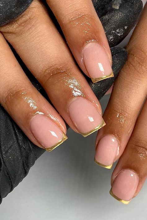 These nails present an elegant take on the classic French manicure with a glossy nude base and striking gold tips. The combination delivers a chic and sophisticated look, perfect for any glamorous occasion.  // Photo Credit: Instagram @gelsbyelisha Nails For 30 Year Olds, French Nails Gold Tip, Short Gold French Tip Nails, Oval Nails Gold, Nude And Gold Nails Short, Golden French Tip Nails, Clear And Gold Nails, Gold Chrome Nails French, Gold Tip Nails French