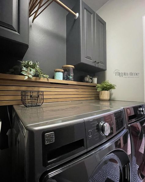 Incredible transformation in just two days! The decision to paint the walls ‘Iron Ore’ from @sherwinwilliams was spot on—it adds a dramatic and modern vibe. The sleek wood slat panel is a perfect way to hide the washer and dryer hookups, and it complements the bold geometric flooring perfectly. This laundry room makeover is seriously one of my favorites. #LaundryRoomMakeover #HomeTransformation #IronOre #SherwinWilliams #ModernDesign #DIYHome #InteriorInspo #LaundryRoomGoals #furnitureartis... Hide Water Lines In Laundry Room, Hide Washer Dryer Hookups, Black And Wood Laundry Room, Laundry Room Water Lines Cover, How To Cover Washer And Dryer Hookups, Dark Grey Laundry Room, Hide Washer And Dryer Hookups, How To Hide Laundry Hookups, Hiding Laundry Room Hookups