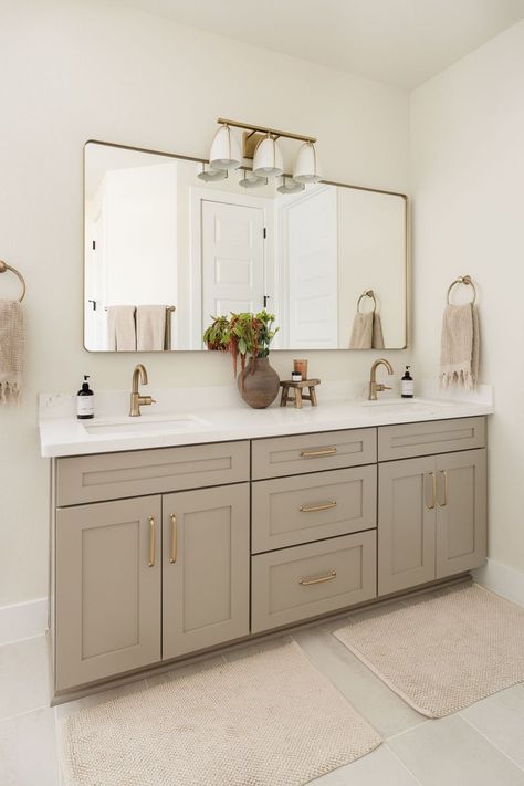 Turned this builder-grade primary bathroom into a relaxing haven. Swapped out the standard black hardware for brass ones. Added a long mirror to span over the vanity instead of two separate ones, and swapped out the light for something unique and refined. Designed by Modern Hippie Design Studio (Austin, Texas) Bathroom Ideas Big Mirror, Double Sink Bathroom Vanity Master Baths, Small Double Vanity Bathroom, Bathroom With White Vanity, Small Double Vanity, Two Sink Vanity, Double Vanity Bathroom Ideas, Primary Bathroom Remodel, Church Bathroom