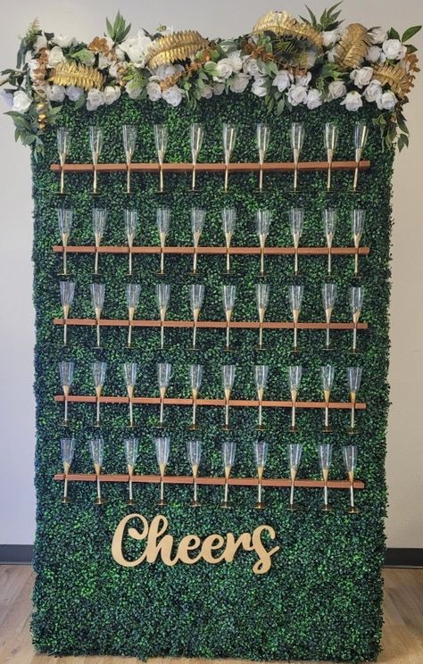 The perfect addition to the party. #partydecor Boxwood hedge wine or champagne wall, with cheers sign attached. Floral decor along the top of the cheers wall. Champagne glasses on the holders. Welcome Drink Wall, Bourbon Party, Cheers Sign, Greenery Wall Decor, Tennis Birthday, Hen Party Decorations, Champagne Wall, Drink Display, Cheer Signs