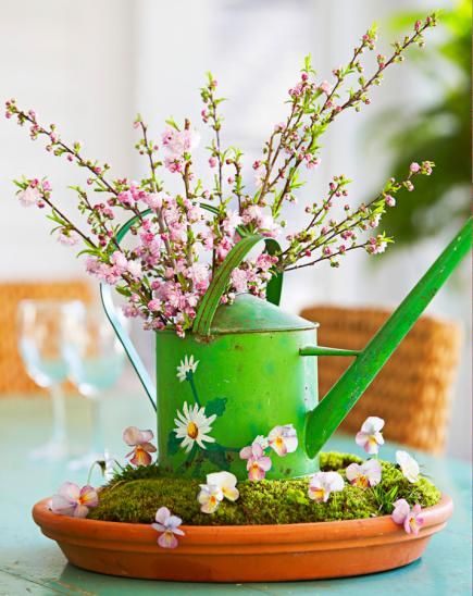 Tabletop Garden: This centerpiece uses a watering can in a large saucer mounded with soil and covered with moss to create a garden feel. Sprigs of violas and branches of flowering almond complete the piece. Tip: When gathering moss for the saucer, lift it in sheets rather than in clumps to create a smoother surface. Watering Can Centerpieces, Flowering Almond, Blooming Branches, Garden Centerpiece, Spring Centerpiece, Spring Tea, Theme Nature, Garden Urns, Moss Garden