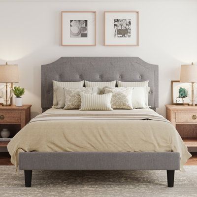 With its scooped headboard and neutral hues, this low-profile platform bed frame brings traditional style to your bedroom. It’s made from steel that’s wrapped in foam-filled upholstery, and it rests on tapered black legs. We love that the included panel headboard has deep button tufting that gives you a cushiony place to lean back and read or watch a movie. Plus, since a box spring isn't required, all you have to do is add the mattress of your choice (sold separately) on top of the system of sla Dark Grey Headboard Bedroom, Gray Headboard Bedroom, Bedroom With Grey Headboard, Gray Headboard Bedroom Decor, Gray Tufted Bed, Gray Tufted Headboard, Neutral Color Bedroom, Grey Headboard Bedroom, Gray Headboard