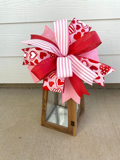 Decorate this Valentines with this gorgeous handmade Valentines Day bow. It measures approximately 10” wide by 4” deep when fluffed. Assembled using a chenille stem and can easily attach to your Valentines Wreath, Valentines lantern decor, or Valentines gift basket. It is made using 2.5” solid pink ribbon, 2.5” pink ribbon with hearts, 1.5” shimmery red ribbon, and 1.5” pink striped ribbon. It it perfect for the season of love! ♥️ The bow shown is approximately 10” wide and 5” in height. Bein Easy Door Wreaths, Valentines Gift Basket, Lantern Bows, Door Hanger Bow, Bow For Wreath, Valentine Gift Baskets, Lantern Decor, Valentines Wreath, Valentines Day Decor