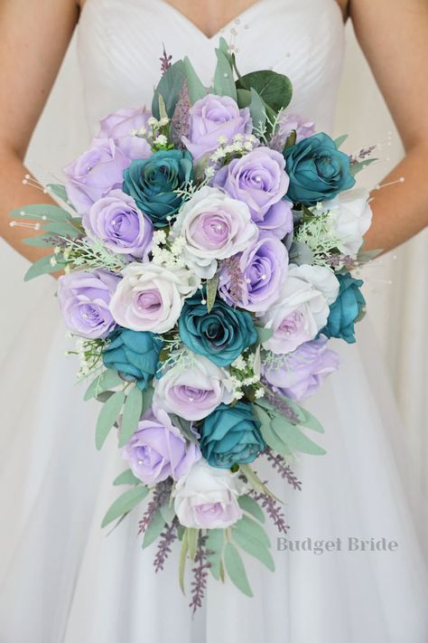 This lovely assortment of is bound to turn heads on your wedding day. This lovely cascading brides’ bouquet from the is an absolutely breathtaking arrangement for any bride to be, in any season. This bouquet is made with lavender roses, lavender center roses, and teal roses accented with greenery This bouquet is 10” wide, 18” long, and is crafted by our in-house florists without using a foam base to anchor the flowers to the bouquet. Instead, we wire our bouquets by hand so that we can further e Teal Lavender Wedding, Blue Purple White Wedding Bouquet, Lilac And Turquoise Wedding, Pastel Rainbow Wedding Flowers, Mint Green And Purple Wedding Theme, Purple And Aqua Wedding, Lilac And Sky Blue Wedding, Teal And Lilac Wedding, Jedi Wedding