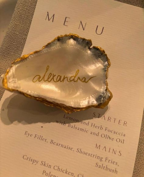 Hi there!  I'm honoured to be considered to be part of your special day.  Each oyster shell is meticulously painted with a beautiful pearl paint,  carefully edged with a rich gold and handwritten with your guests names. I personally collect each shell to ensure the highest quality for your event.  I have a few options for your order that you can select below: - Pearl Shell - Your oyster shell painted with pearl paint only.  - Pearl Shell with Name - Your oyster shell painted with pearl paint onl Oyster Place Setting Wedding, Tropical Place Cards Wedding, Oyster Shell Wedding Place Cards, Oyster Themed Party, Oyster Wedding Decor, Oyster Shell Painting, Oyster Name Cards, Wedding Oysters, Oyster Shell Wedding