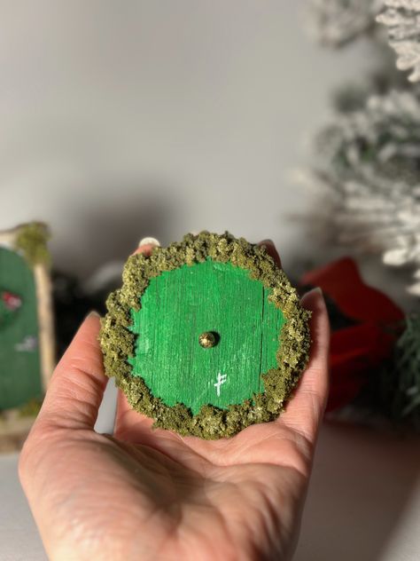 These unique mini Hobbit doors are carved and hand-painted, decorated around a grapevine wreath with moss, faux foliage, and an antique (color) brass knob. Perfect as a Christmas tree ornament or even a subtle decoration to your living room, office, or bedroom! This art piece is delicate and fragile and to be handled with care. Hobbit Decor, Hobbit Doors, Lord Of The Rings Gift, Hobbit Door, Door Ornament, Brass Knob, Brass Knobs, Handmade Ornaments, Christmas Tree Ornament