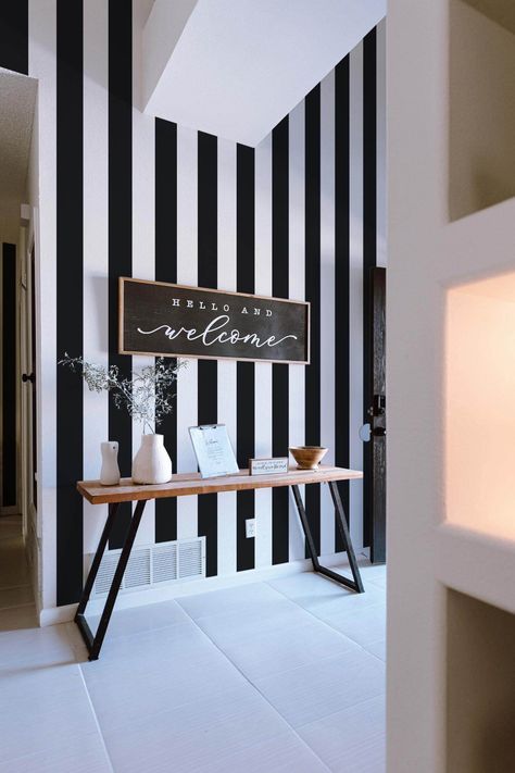 This black and white striped wallpaper pattern is the perfect choice to add a new design element in your hallway/entryway, for a couple of reasons: its neutral colors give you the ability to change your décor and furniture around it as you see fit (with the wallpaper still accentuating the space beautifully), but it is also a pattern that has been a top trend for quite some time (and its not slowing down any time soon). Choosing a wallpaper design can be intimidating because we all want that pat Black White Stripes Wallpaper, Wall Slat Wallpaper, White Rooms With Accent Wall, Black And White Paneling, Living Room Decor With Wallpaper, Black Ceiling Entryway, Edgy Salon Interior Design, Black And White Salon Decor, Black And White Hallway Ideas