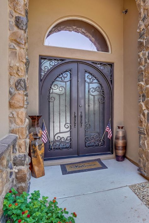 Nothing completes romantic old-world design like iron details. To get a classic Mediterranean look, you should go with scrolling or floral patterns. Read more on our blog!  #mediterraneandecor #mediterraneanhomes #irondoor #wroughtiron #homedecor #homeinspiration Mediterranean Style Front Door, Single Entry Iron Front Door, Mediterranean Front Doors, Iron Front Door Single Rustic, Arched Iron Front Door Single, Entrance Ideas Entryway, Arched Entry Doors Pinky’s Iron Doors, Wrought Iron Doors Front Entrances, Double Front Entry Doors