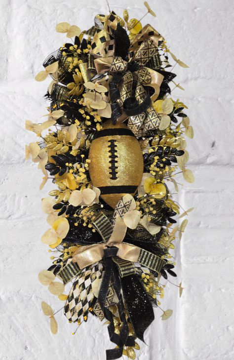 Get ready for the season with this stunning Football-Themed Fall Wreath! Perfect for football fans and game-day gatherings, this handcrafted wreath features rich black and gold hues, glittering accents, and bold ribbons, topped with a sparkling football centerpiece. Whether you're decorating your front door, porch, or game room, this wreath will add a festive touch to every kickoff. Celebrate your team spirit in style with a wreath that's as vibrant as your love for the game! Football Centerpiece, Steelers Wreath, Football Centerpieces, Football Wreaths, Football Wreath, Front Door Porch, Door Porch, Door Swag, Door Wreath Hanger