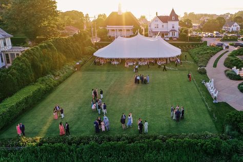 Drone shot of outdoor, tented Ocean House wedding in Watch Hill, Rhode Island. Guests enjoying cocktail hour on the lawn at sunset Floral Design: Hana Floral Design @hanafloral Photographer: Clark Brewer https://www.clarkbrewerphotography.com Small Backyard Party, Sperry Tents, Puglia Wedding, Wedding Marquee, Oyster White, Rhode Island Wedding, Pennant Flags, Ocean House, Tent Reception