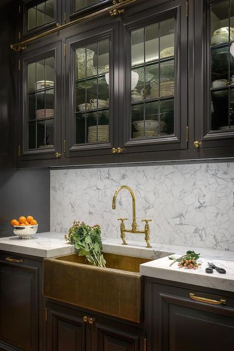 Black galley kitchen features glass front upper cabinets fitted with a brass ladder rail and black lower cabinets adorned with brass hardware paired with gray and white marble countertops and backsplash. Black Galley Kitchen, Black Lower Cabinets, Farmhouse Kitchen Cabinet Decor, Kitchen With Marble, Kitchen Chandelier, Black Kitchen Cabinets, Farmhouse Kitchen Cabinets, Kitchen Cabinets Decor, Classic Kitchen