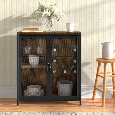 Organize and display your wine collection in style with this 2-door bar cabinet. Whether you’re a collector, connoisseur, or just love to have some good vino on hand, you’ll appreciate all the storage and the contemporary-meets-industrial styling of this piece. It is made from engineered wood that’s finished in two tones of rustic brown and black and has a black metal frame. The two doors have mesh fronts that allow for ventilation while adding a distinctive contrast and visual texture. Inside i Bar Console Cabinet, Bar Cabinet Styling, Wine Cabinet, Bar Cabinet Ideas, Wine Glass Cabinet, Liquor Cabinet Bar, Wine Rack Table, Armoire Bar, Wine Storage Cabinets