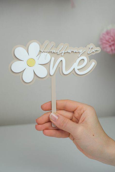 Daisy Cake Topper | Halfway To One + Name Charm Daisy themed cake topper made from double layered 3mm acrylic. High quality product. The set includes:  Daisy Cake Topper + Name charm Can be bought separately   The flower will be white and lemon, and the text will be white. You get to choose the color for the back layer (Desert Beige Matte on a photo) Size of topper is approx. 15cm wide - 6" and about 14- 15cm high (including a stick)   Feel free to tag me on instagram @twinkled3cor :) Because this product is customized for each individual, every item is created upon order placement. As a result we do not provide options for returns, exchanges, or refunds. Once we hand over your order to the shipping couriers, we are not responsible for items lost or delayed in transit, however, if your ord Daisy Half Birthday, Layered Deserts, Halfway To One, Daisy Cake Topper, Half Way To One, Half Birthday Cakes, Daisy Cake, Daisy Cakes, Birthday Topper