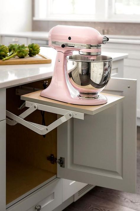 A pink KItchenAid Mixer sits atop a pop up shelf fixed beneath a white island finished with white cabinets adorned with polished nickel knobs. Pink Kitchenaid Mixer, Pink Kitchenaid, Kitchen Island Design Ideas, Best Kitchen Island, Island Design Ideas, Outdoor Kitchen Appliances, Kitchenaid Mixer, Kitchen Island Decor, Modern Kitchen Island