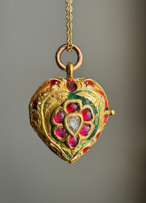 Rooted in Hindu mythology, the parrot is considered a messenger of Lord Kama, The God of Love, given the bird's capacity to imitate human speech. Symbolically, these parrots represent fertility and desire due to their colorful plumage. The red is symbolic of desire, and the green fertility and new life.  This late 19th century heart-shaped locket has been beautifully crafted in 22 karat gold. The locket has been hand engraved and displays a pair of vibrant enameled a parrots framing a gem-set flower head filled with candy apple red rubies, bright green emeralds and polki diamonds.    Weight: 4.6 dwt Measurements: 18.5 mm x 19.5mm (without bail), 27 mm with the bail Condition notes: There is extensive loss to the enamel. The bail is a later addition to the locket and is 14 karat gold Markin God Of Love, Ruby Heart, Kundan Set, Hindu Mythology, Body Adornment, Candy Apple Red, Heart Locket, Locket Necklace, Hand Engraving