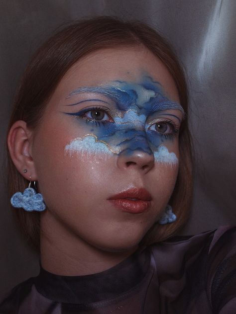 In the middle of the face are drawn blue clouds, that are outlined in gold Weather Makeup Looks, Sky Face Paint, Cloud Eye Makeup, Rain Makeup, Surrealist Ball, Cloud Makeup, Sky Makeup, Makeup Painting, Air Makeup